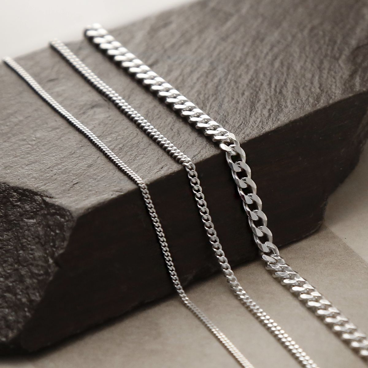 Heavy, medium and fine sterling silver curb chains on draped on wooden beam