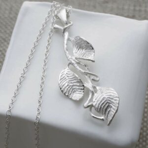 silver three leaves on branch pendant necklace laid on pot