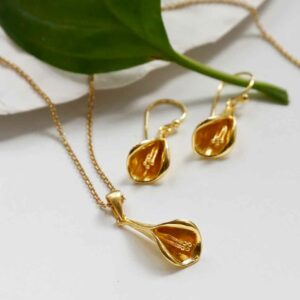 Gold Calla Lilly Necklace and earrigns on background with green leaf