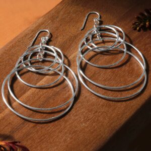 Multiple shiny silver rings hanging on hooks laying on a dark wooden background