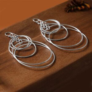 Multiple shiny silver rings hanging on hooks laying on a dark wooden background