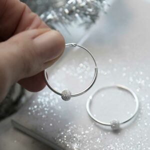 Models hand showing Sterling silver disco ball hoops on sparkly tile background