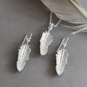 small dangly feather earrings and pendant on grey background with a feather