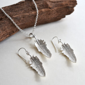 small dangly feather earrings and pendant on white background draped over wood