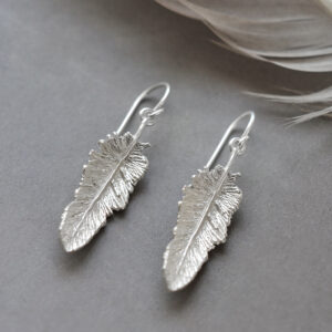 small dangly feather earrings on grey background with a feather