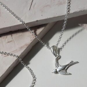 Sterling Silver Swallow Necklace on Pastel Pink Background with Harsh Shadows