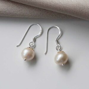 Sterling silver round pearl dangly Earrings on a white background with a cream cloth