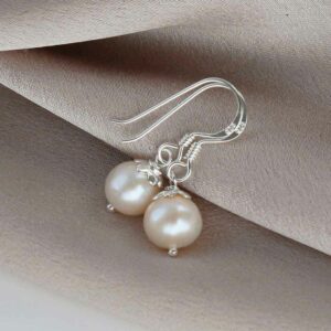 Sterling silver round pearl dangly Earrings on a white background with a cream cloth