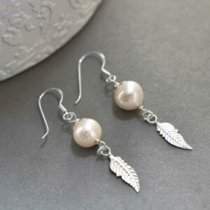 Feather and pearl earrings on grey background