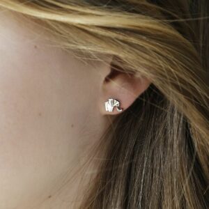 A silver geometric elephant stud in a girls ear surrounded by blonde and brown hair pushed away from the earring