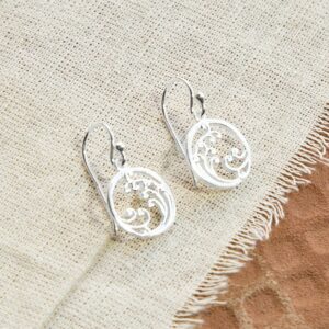 Silver drop earrings with wave details, laid out on a canvas background with terracotta tile