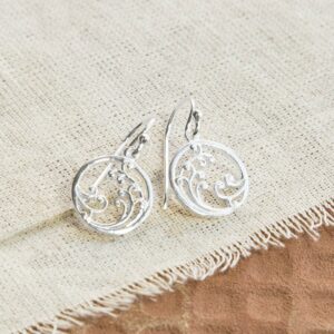 Silver drop earrings with wave details, laid out on a canvas background with terracotta tile