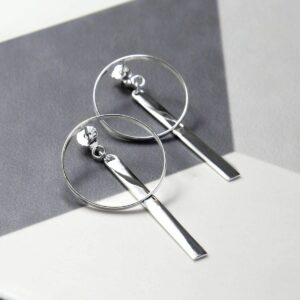 Large circular silver earrings with a long silver bar dangling from the top of them with a grey background