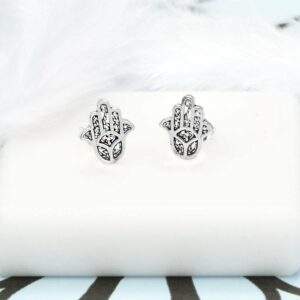 Pair of Silver Hamsa Hand Studs on white tile background and blue and black pattern paper with White Feather