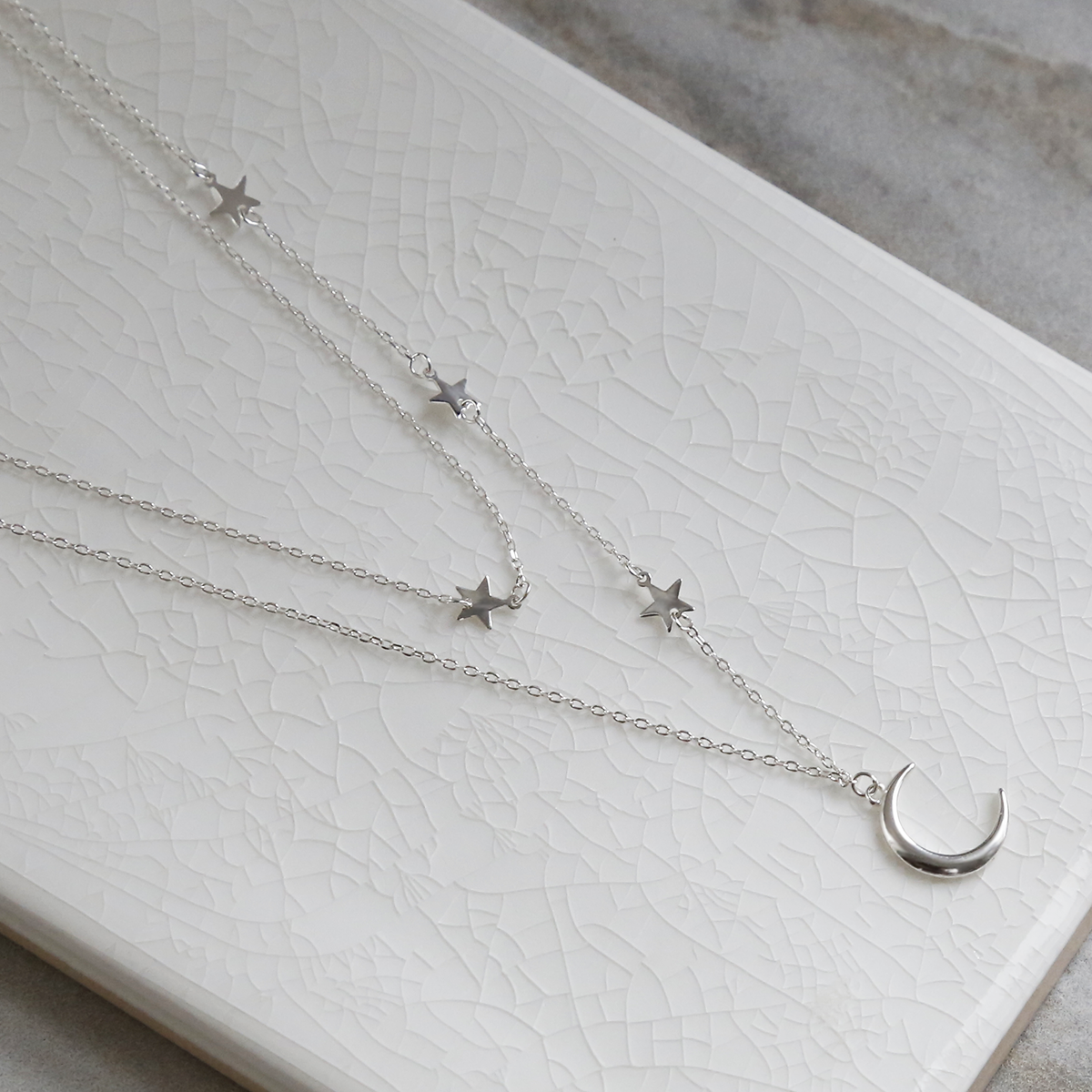 Double layered sterling silver moon and star charm necklace on white background with close up of crescent moon.