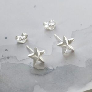 A pair of sterling silver solid star studs sat on a white marble background