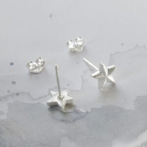 A pair of sterling silver solid star studs sat on a white marble background