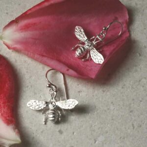 sterling silver dangly bee earrings laid out with petals