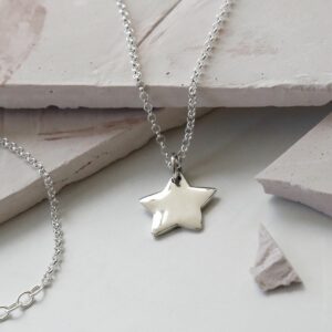 Sterling Silver Polished Star Necklace Hanging over slate with a chain