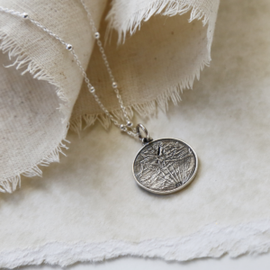 Sterling Silver Roman Head Coin Necklace hanging on linen