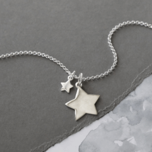 DOUBLE STAR NECKLACE ON A GREY BACKGROUND ENGRAVING REMOVED.
