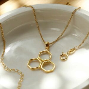 gold triple hexagon honeycomb pendant on gold chain in sunlit bowl