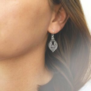 model shot wearing dangly sterling silver earring with intricate detailing.