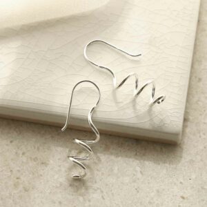 silver bold coil drop earrings leaning on white tile