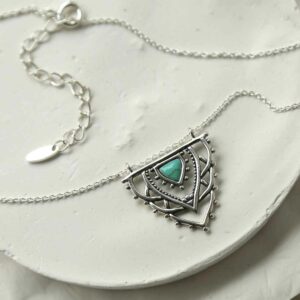 silver exotic necklace with turquoise triangle strewn on tile