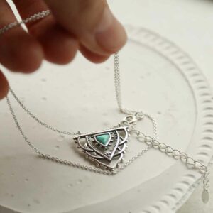 silver exotic necklace with turquoise triangle laid on tile