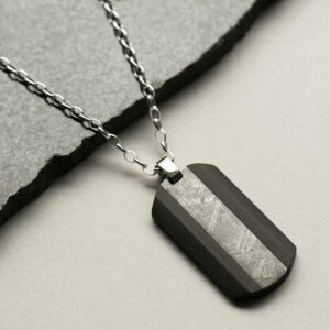 Meteorite and carbon fibre dog tag necklace laid on stone