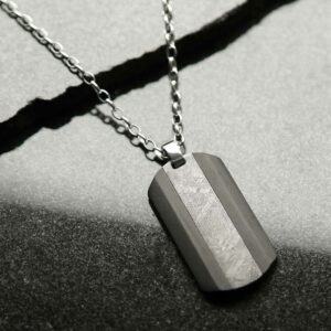 Meteorite and carbon fibre dog tag necklace on stone background with shadow