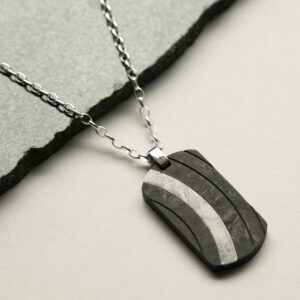 Meteorite and carbon fibre curve dog tag necklace laid on stone