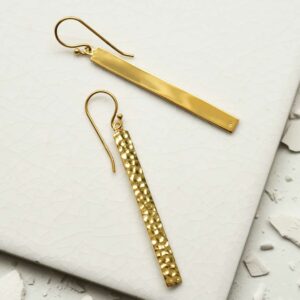 gold dangly straight earrings on a white tile