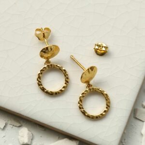 a pair of gold circle stud earrings on a white tile