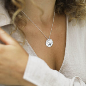 single blue topaz gem in centre of hammered pendant on model