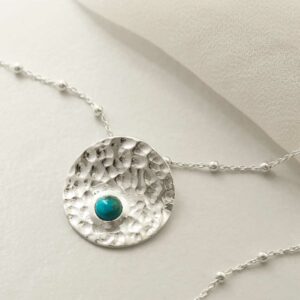 single turquoise gem in centre of hammered pendant on model