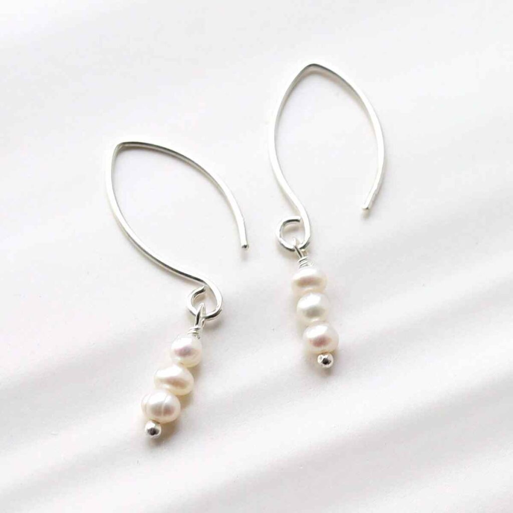 silver drop earrings with three hanging pearls on tile in sunlight