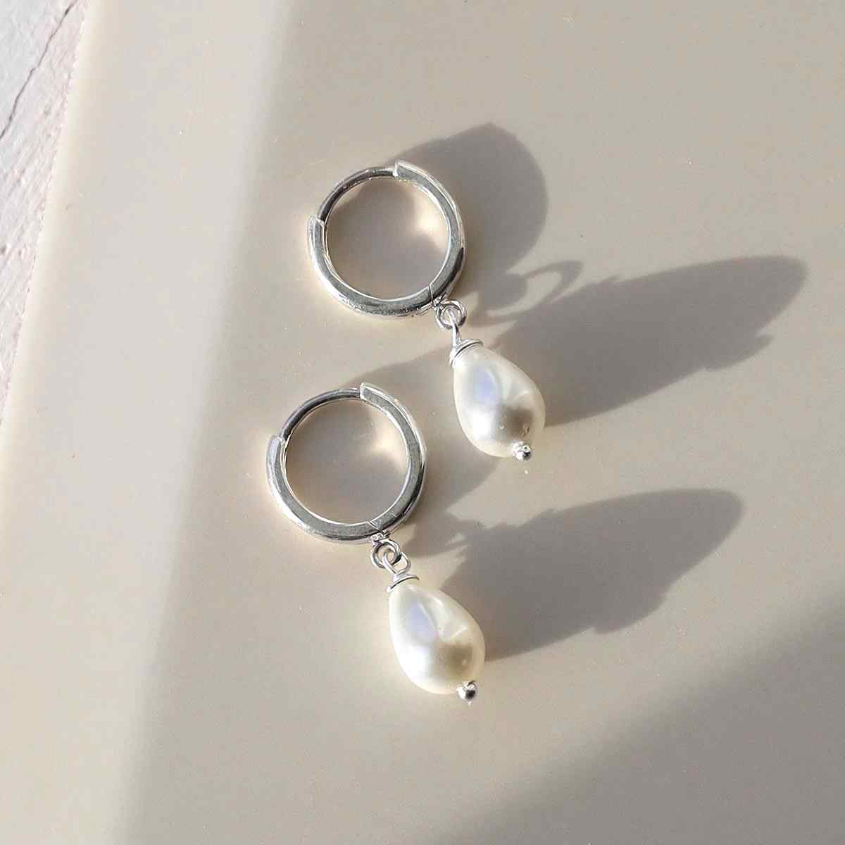 silver huggie hoops with a hanging pearl in sunlight