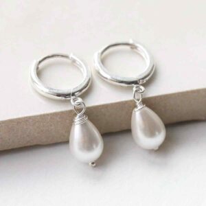 silver huggie hoops with a hanging pearl leaning on tile