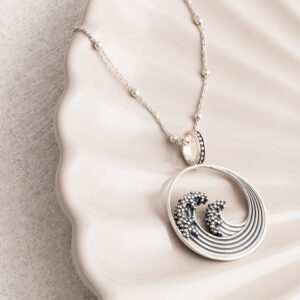 Sterling silver necklace with a ball chain inspired by the iconic Great Wave off Kanagawa, featuring intricate oxidised detailing to highlight the wave’s movement and texture on a cream shell background.