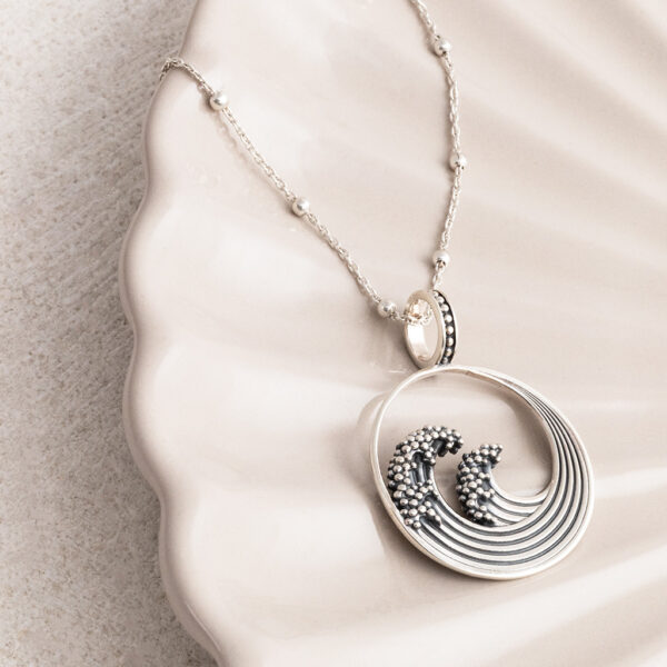 Sterling silver necklace with a ball chain inspired by the iconic Great Wave off Kanagawa, featuring intricate oxidised detailing to highlight the wave’s movement and texture on a cream shell background.