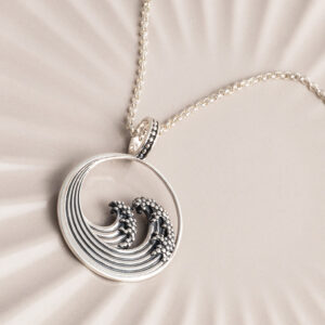 Sterling silver necklace inspired by the iconic Great Wave off Kanagawa, featuring intricate oxidised detailing to highlight the wave’s movement and texture on a cream shell background.