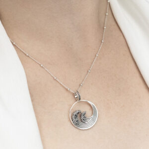 Sterling silver necklace inspired by the iconic Great Wave off Kanagawa, featuring intricate oxidised detailing to highlight the wave’s movement and texture worn by a model with a white blouse.