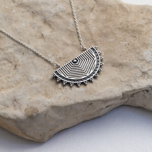 Sterling silver geometric half moon necklace featuring a boho oxidised finish on a stone background.