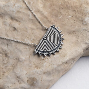 Sterling silver geometric half moon necklace featuring a boho oxidised finish on a stone background.