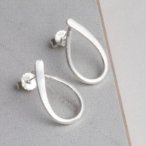 Sterling silver ribbon loop stud earrings with a delicate twisted design, shown on a grey tile background.