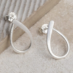 Sterling silver ribbon loop stud earrings with a delicate twisted design, shown on a grey tile background.