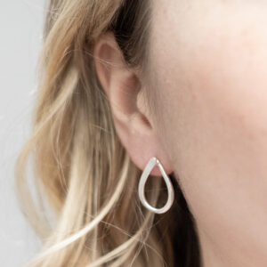 Sterling silver ribbon loop stud earrings with a delicate twisted design, worn by a model with curly blonde hair.