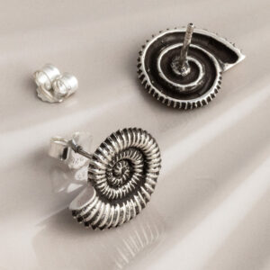 Sterling silver stud earrings featuring fossil-inspired designs with an oxidised finish, highlighting the intricate spiral patterns. A unique, nature-inspired accessory with a vintage, textured look on a cream shell background.